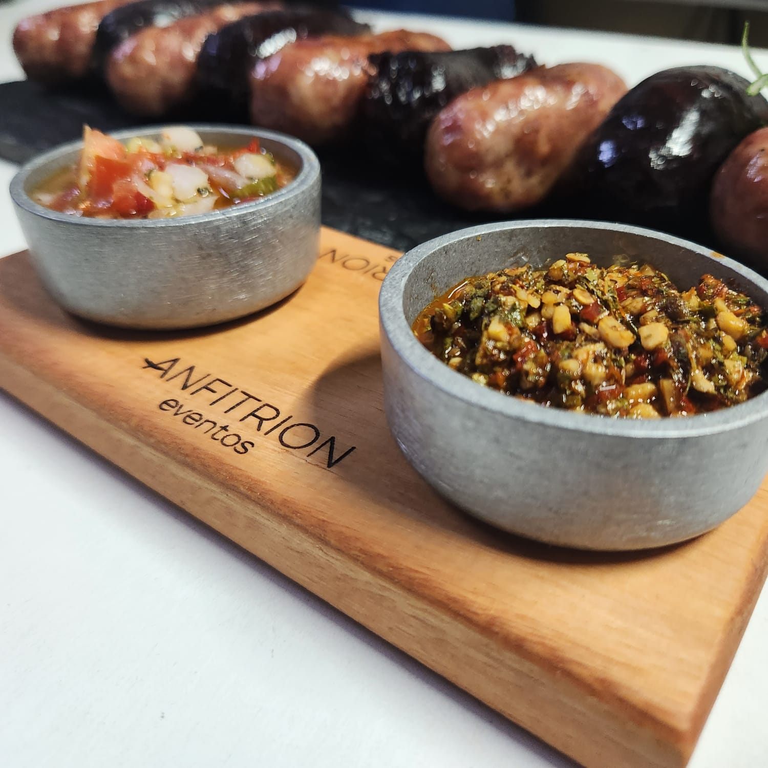 Tabla de achuras con chorizo, morcilla, chimichurri y salsa criolla, con la marca Anfitrión eventos